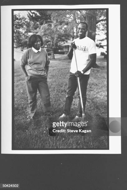 St. Louis high school football coach Robert Shannon smiling, holding rake outside home w. Wife, Jeannette.
