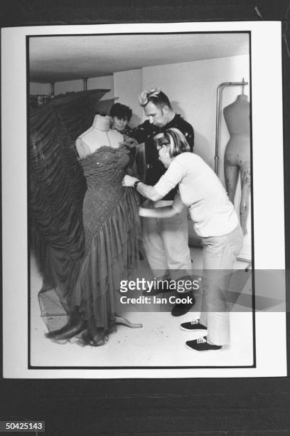 Fashion designer Jean-Paul Gaultier working w. His two female assistants as they drape mannequin w. One of his new evening dress creations in cutting...