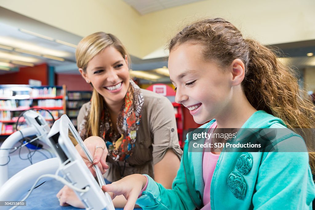 Librarian helping elementary student use digital tablet in library