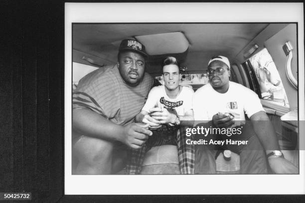 Rap singer Vanilla Ice sitting between his bodyguards Big E & Chilly in back seat of limousine during publicity tour.