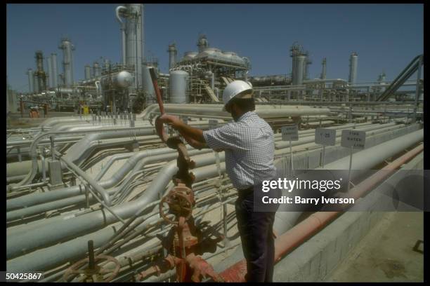 Worker dwarfed by sprawling network of pipelines & storage tanks at Saudi Aramco oil refinery & loading terminal at Ras Tanura, Arabia.