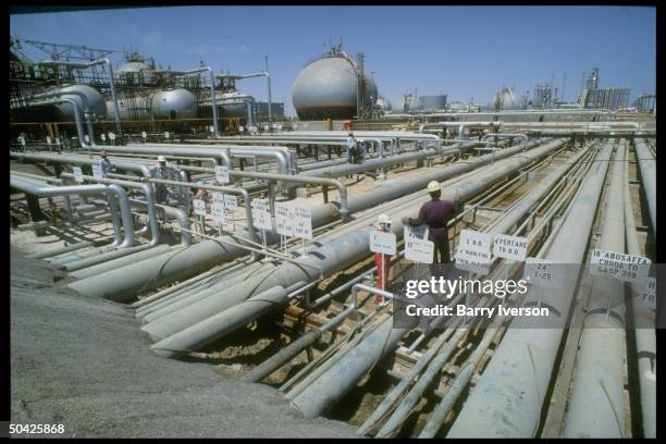 Worker dwarfed by sprawling network of pipelines & storage tanks at Saudi Aramco oil refinery & loading terminal at Ras Tanura, Arabia.