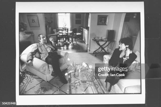 Author Philip Roth sitting in easy chair, chatting w. His wife actress Claire Bloom in r living room at home.