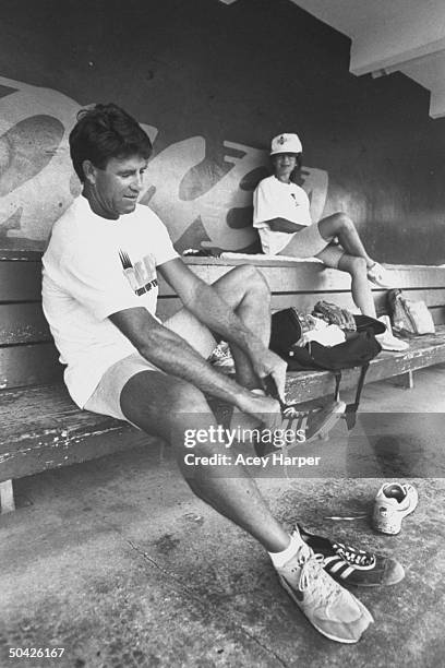 Former baseball pitcher Jim Palmer in dugout w. 2nd wife, Joni, changing sneakers during practice for comeback into the game professionally at age...