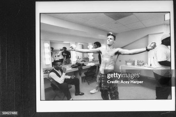 Rap singer Vanilla Ice bare-chested, flexing his muscles in dressing room as 3 unident. Black men meander aimlessly backstage at Miami Arena before a...