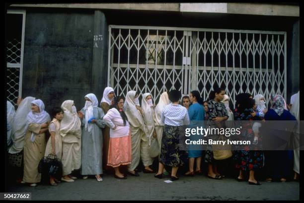 Women & girls, some modestly veiled, Moslem-style, lining up, waiting outside govt-subsidized store to buy food.