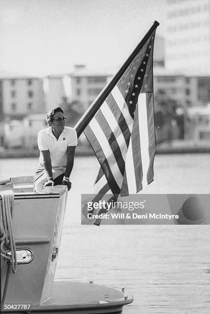 Singer, businessman Jimmy Dean posing on the rail next to an American flag on pole at the stern of his yacht.
