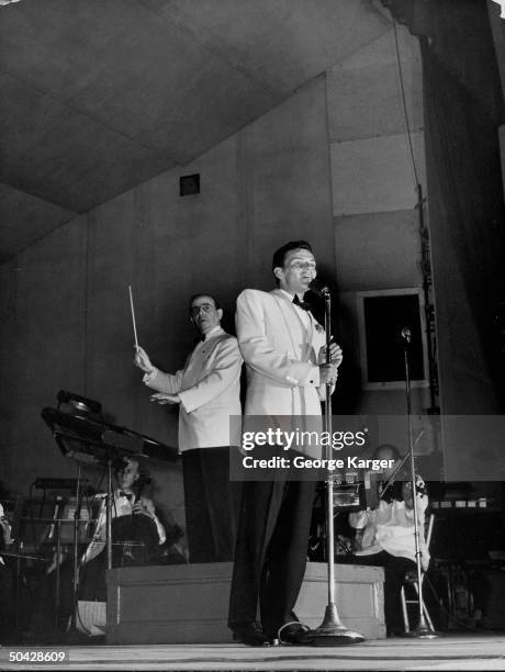 Singer Frank Sinatra rendering a song as conductor Max Steiner leads the New York Philharmonic orchestra during concert featuring the crooner which...