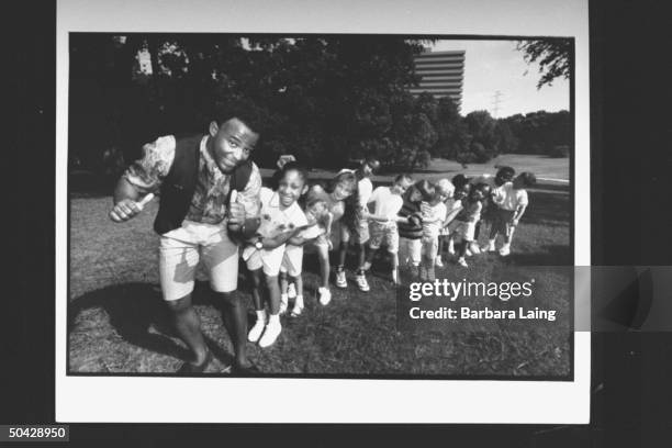 Actor David Joyner, who plays Barney the lovable purple dinosaur on the PBS program Barney & Friends, marching in front of a train of boys and girls...