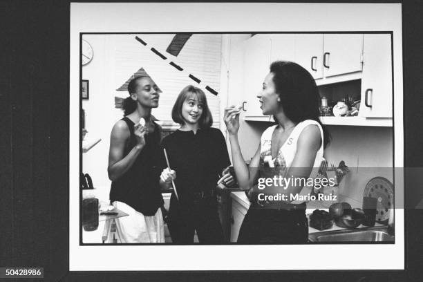 Actress Tamara Tunie nibbling on snacks w. Her friends Dwania Kyles and Susan Marie Snyder in the kitchen at home.
