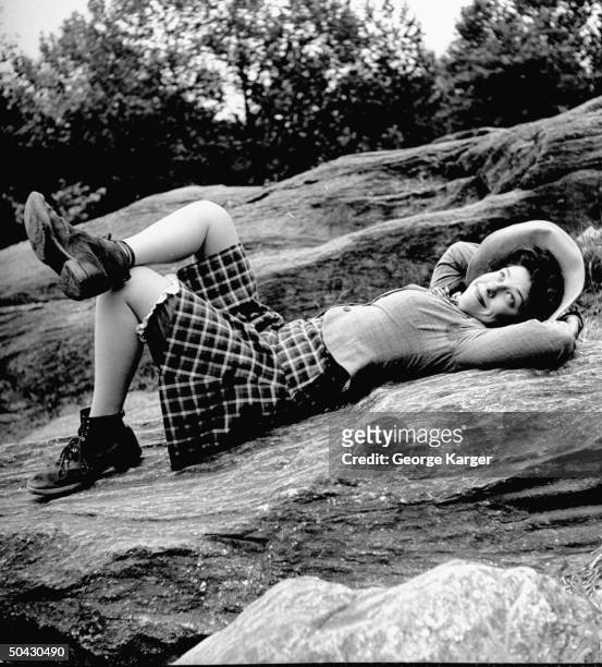 Singer Judy Canova lying on rocks wearing lace-up work boots, bloomers under her short skirt and hat.