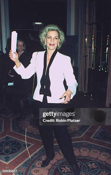 Actress Lauren Bacall raising a rolled-up program in her right hand as she poses at Museum of the Moving Image party in honor of actor Al Pacino at...