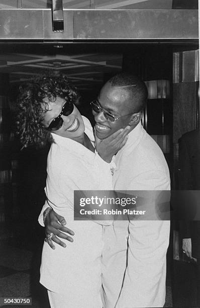 Married singer Whitney Houston and Bobby Brown wearing sunglasses and hugging after her concert.