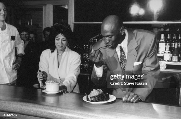 Chicago Bulls basketball star Michael Jordan sampling steak and potatoes dish while standing next to wife Juanita at bar at the opening of his...