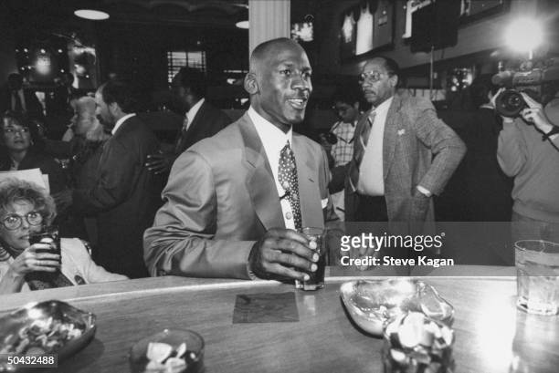 Chicago Bulls basketball star Michael Jordan holding drink while sitting at bar nr. Others at the opening of his restaurant.