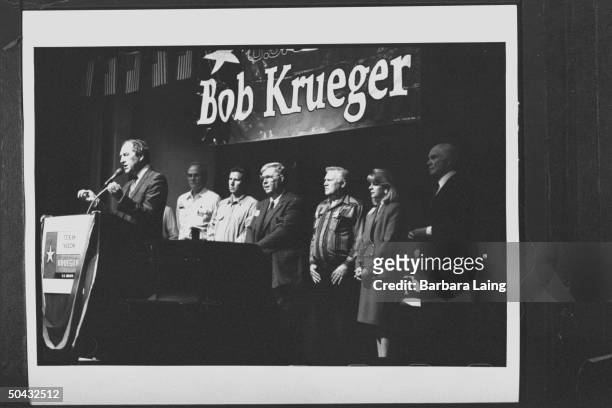 Sen. Bob Krueger speaking into mikes at podium, as wife Kathleen Tobin Krueger, OH Sen. John Glenn and five others look on at campaign stop at the...