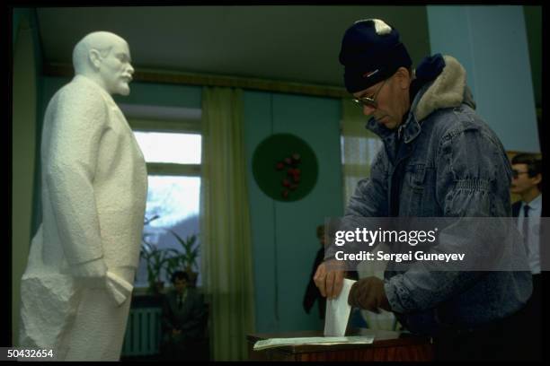 Man inserting ballot in box, watched over by Lenin statue, voting in 1st democratic parliamentary elections at 55th district polls.
