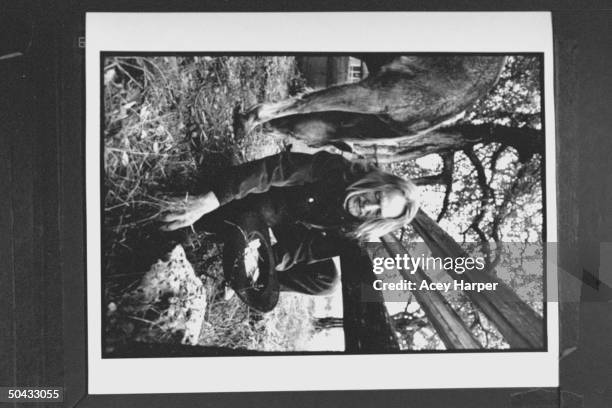 Musician Willie Nelson stooping as he picks up pieces of a broken bottle & places it in his cowboy hat in corral nr. A friend's quarterhorse at his...