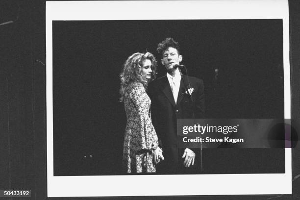 Crooner Lyle Lovett singing into mike nr. His actress bride Julia Roberts during concert at the Deer Creek Music Ctr., on their wedding day.