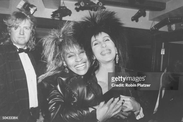 Singer Cher Bono sporting braces on her teeth, happily getting hugged by singer Tina Turner as Turner's mgr. Roger Davies looks on at MTV awards...