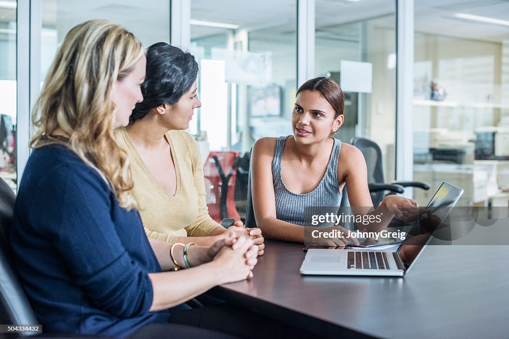 Three multiracial women using laptop computer in modern office