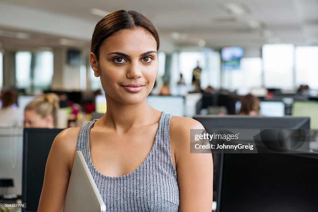 Businesswoman with tablet smiling towards camera in modern office