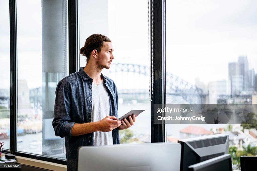 Casual young businessman with tablet by window in modern office