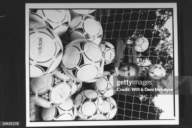 Univ. Of NC soccer forward Mia Hamm sitting amid a dozen or more soccer balls at entrance to goal keeper's net on field on the univ's campus; Chapel...
