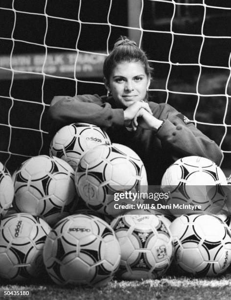 Univ. Of NC soccer forward Mia Hamm sitting amid a dozen or more soccer balls at entrance to goal keeper's net on field on the univ's campus; Chapel...