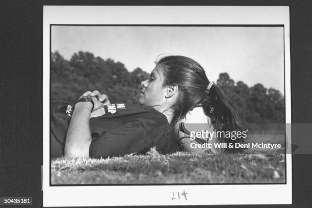 Univ. Of NC soccer forward Mia Hamm using soccer ball to prop up her head as she lies in field during break in practice on the univ's campus; Chapel...
