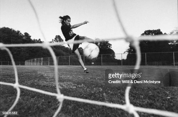 Univ. Of NC soccer forward Mia Hamm kicking soccer ball into net during practice, in field on the univ's campus; Chapel Hill.
