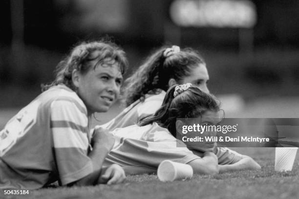 Univ. Of NC all-American soccer player Mia Hamm flanked by two unident. Teammates as she lies on soccer field nr. Empty paper cups during break in...