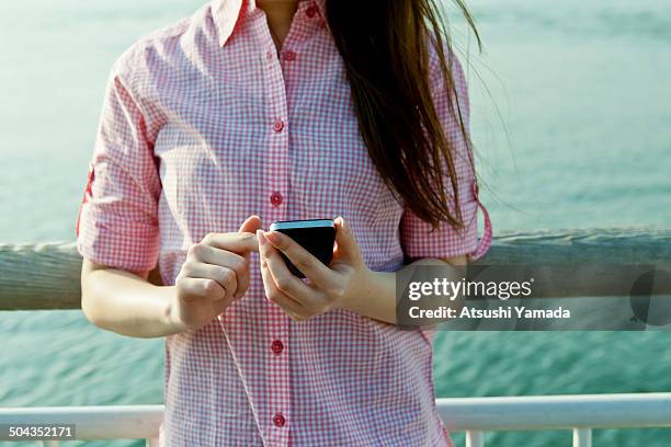 young woman using smartphone at riverside - feature phone stockfoto's en -beelden