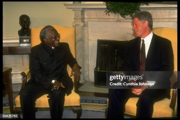 Pres. Bill Clinton mtg. W. S. African Archbishop Desmond Tutu in WH Oval Office, sharing laugh, sitting in front of Swedish ivy-topped fireplace.