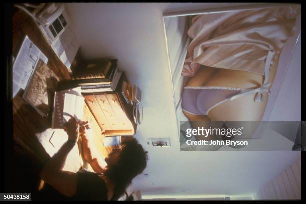 Actor Sylvester Stallone sitting in home office writing w. Painting entitled Reina With Lace Pants by John Kacere on wall.