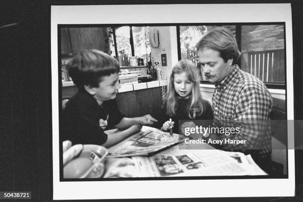 Former actor Jon Provost reading newspaper w. Daughter Katie & son Ryan as they sit at kitchen table at home.