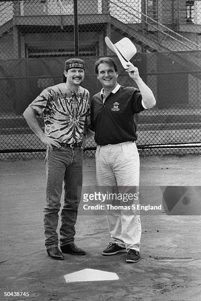 Musician Tim McGraw w. Father, former baseball player Tug McGraw, as they pose sporting each other's signature hats while standing on baseball field.