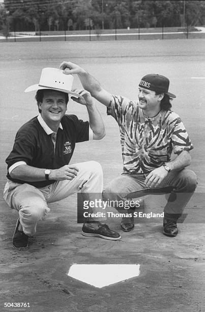 Musician Tim McGraw w. Father, former baseball player Tug McGraw, wearing each other's signature hats as they crouch nr. Homeplate on baseball field.