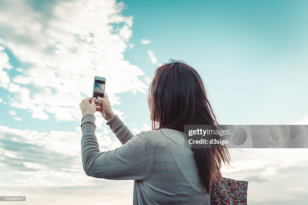 Female taking photo of blue sky by smartphone