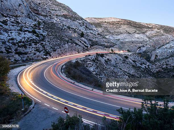 lights of vehicles circulating along a road with curves to the dusk - car light trails stock pictures, royalty-free photos & images