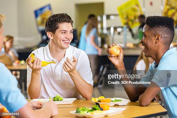 high school boys laughing together while eating lunch in cafeteria - boy packlunch stockfoto's en -beelden