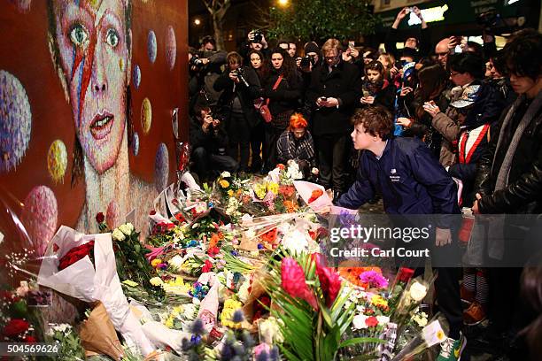 Boy leaves flowers beneath a mural of David Bowie in Brixton on January 11, 2016 in London, England. British music and fashion icon David Bowie died...