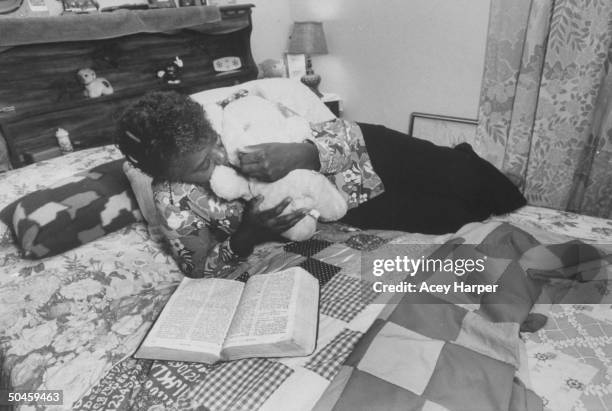 Annie Mae Richardson, wife of convicted murderer of 7 of their children in 1967 who she believes is innocent, reading Bible & holding onto stuffed...
