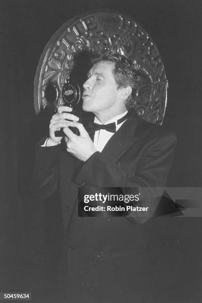 Actor Michael Crawford kissing Tony Award he won for his performance in The Phantom of the Opera during after- ceremony party at Sardi's restaurant,...