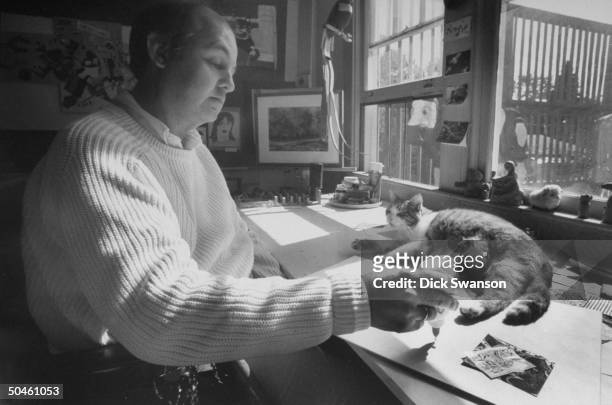 White House Press Secretary James Brady working on an art project at the home of artist friend Wendy Maiorana with a cat nearby.