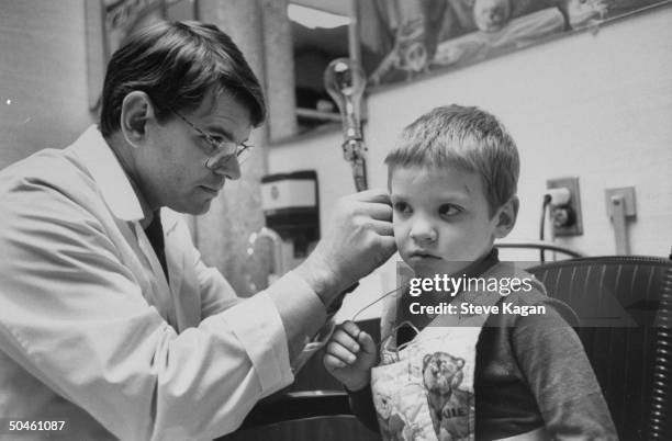 Four year old Timmy Brandau, recipient of a coclear implant, which allows him to hear for the first time, wearing a hearing aid, being examined by...