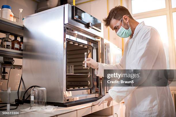 scientist about to put a test tube into sterilizer. - young man scientist stock pictures, royalty-free photos & images