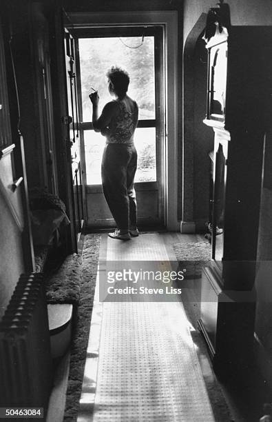 Daughter of Frank Reed silhouetted by door w. Back to camera holding cigarette, re: father who was kidnapped by Islamic Jihad.