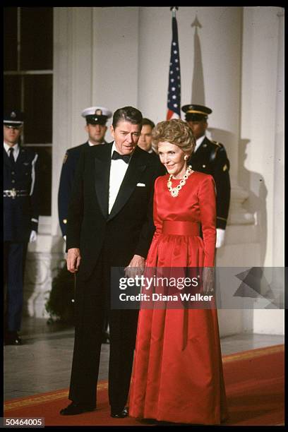 Elegantly garbed Pres. & Nancy Reagan holding hands, poised on red carpet, during State Dinner in honor of Brtish PM.