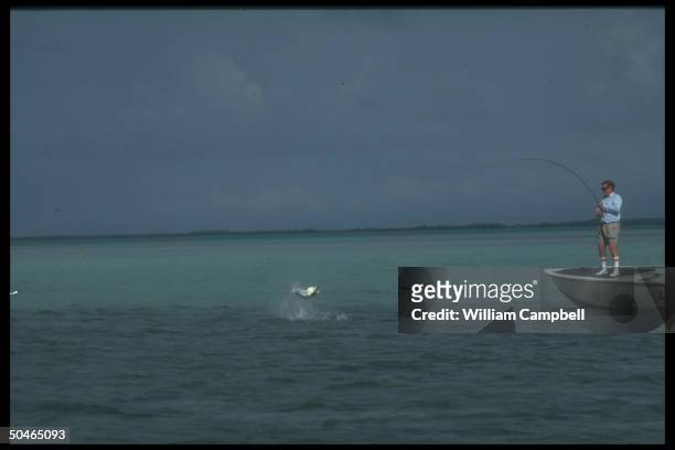 Art Critic Robert Hughes landing a tarpon fish while standing on boat fly fishing.